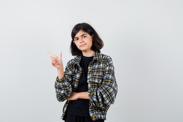 Little girl in t-shirt, jacket pointing to the left side and looking confident , front view.