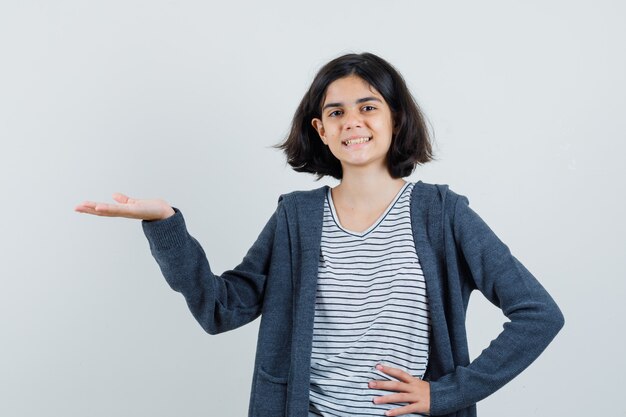 Little girl in t-shirt, jacket pretending to hold or show something and looking jovial ,