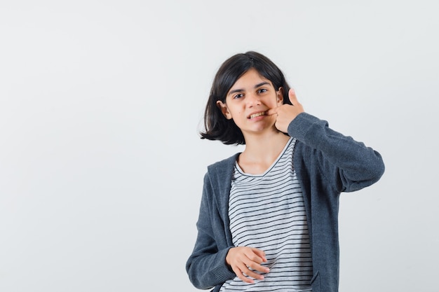 Little girl in t-shirt, jacket showing thumb up and looking glad