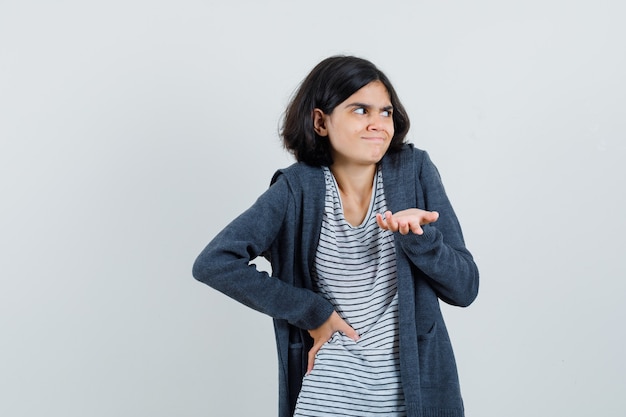 Little girl in t-shirt, jacket stretching hand in puzzled gesture ,