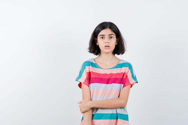 Little girl in t-shirt,  jeans holding hand on arm and looking surprised , front view.