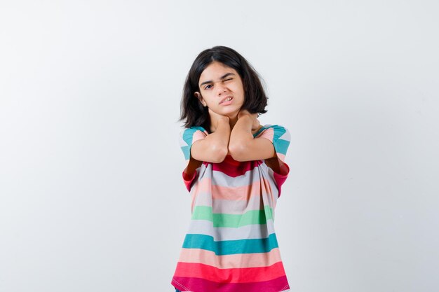 Little girl in t-shirt, jeans holding hands on neck, having neck pain and looking exhausted , front view.