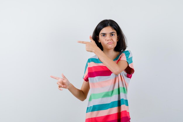 Little girl in t-shirt,  jeans pointing left with index fingers and looking displeased , front view.