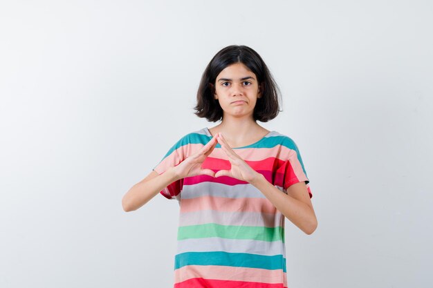 Little girl in t-shirt, jeans showing insurance gesture and looking displeased , front view.