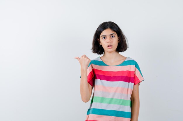 Little girl in t-shirt, jeans showing thumb up and looking surprised , front view.