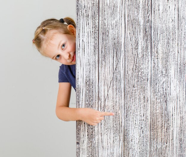 Little girl in t-shirt pointing finger at something and looking glad , front view.