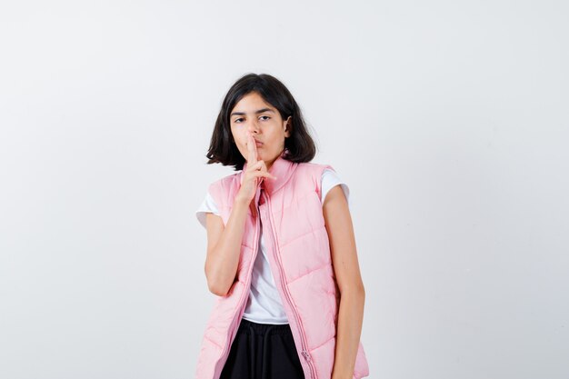 Little girl in t-shirt and puffer vest showing silence gesture