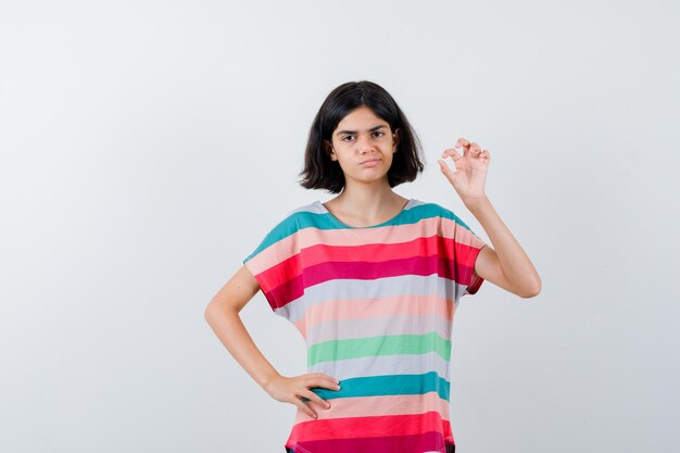 Little girl in t-shirt showing ok gesture and looking serious , front view.