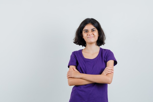 Little girl in t-shirt standing with crossed arms and looking cheery ,