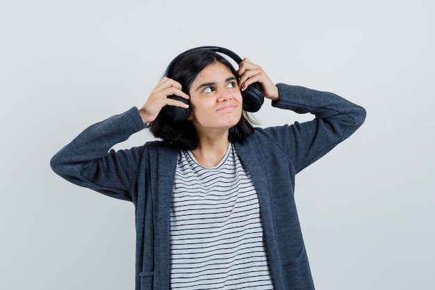 Free photo little girl taking off headphones in t-shirt, jacket and looking curious