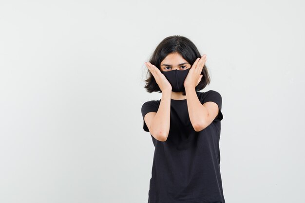 Little girl touching face skin in black t-shirt, mask , front view.