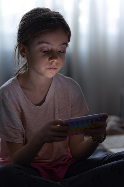 Little girl uses the phone while sitting in bed in the evening