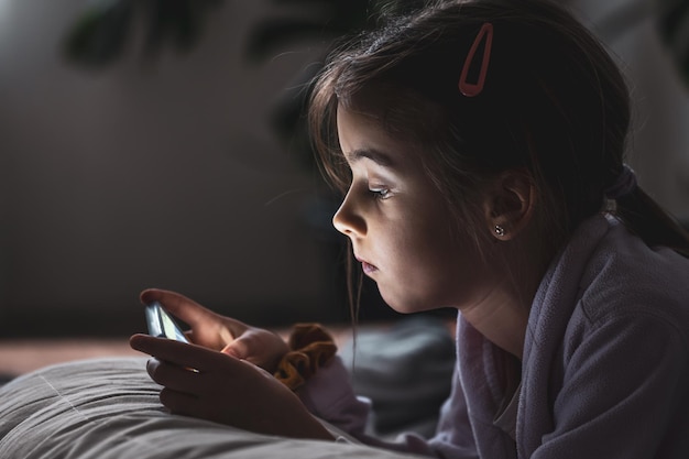 Little girl uses a smartphone lying on the pillow at home