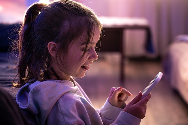 Free photo a little girl uses a smartphone while sitting in her room