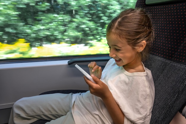 Маленькая девочка пользуется смартфоном, сидя в поезде