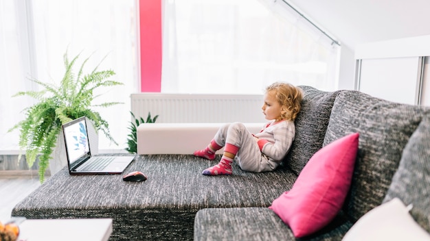 Free photo little girl watching movie on sofa