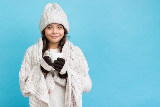 Little girl wearing blanket and holding cup with tea