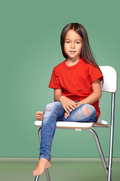 Free photo little girl wearing red t-short and posing on chair on green background