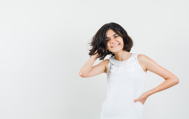 Little girl in white blouse holding hand in hair and looking pretty , front view.