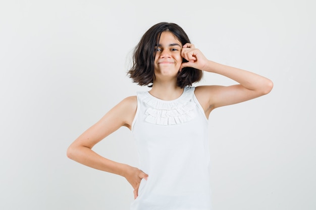 Little girl in white blouse posing while standing and looking cheerful , front view.