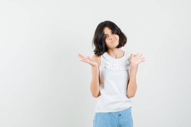 Little girl in white blouse, shorts showing helpless gesture and looking confused , front view.