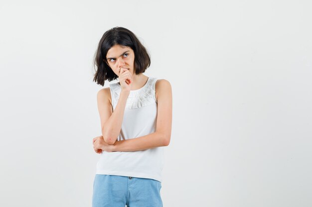 Little girl in white blouse, shorts standing in thinking pose and looking sensible , front view.