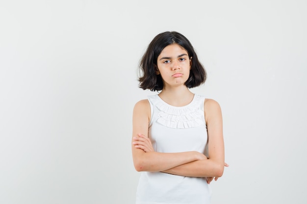 Little girl in white blouse standing with crosses arms and looking upset , front view.