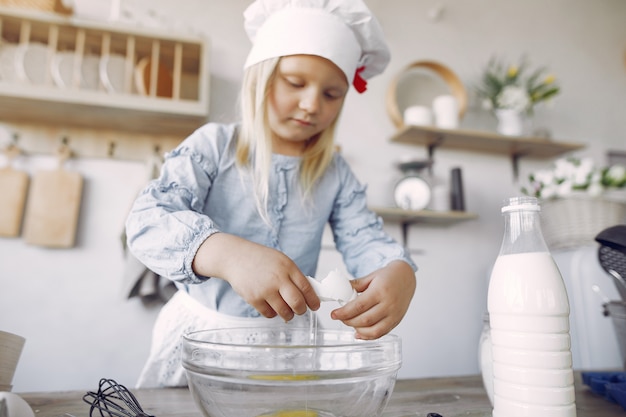 Little girl in a white shef hat cook the dough for cookies