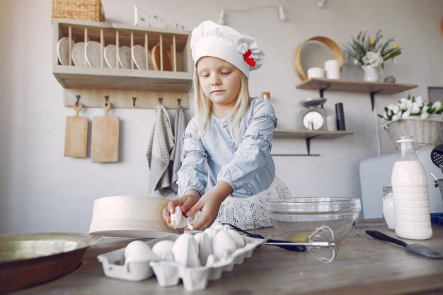 白いシェフの帽子の少女がクッキーの生地を調理します。