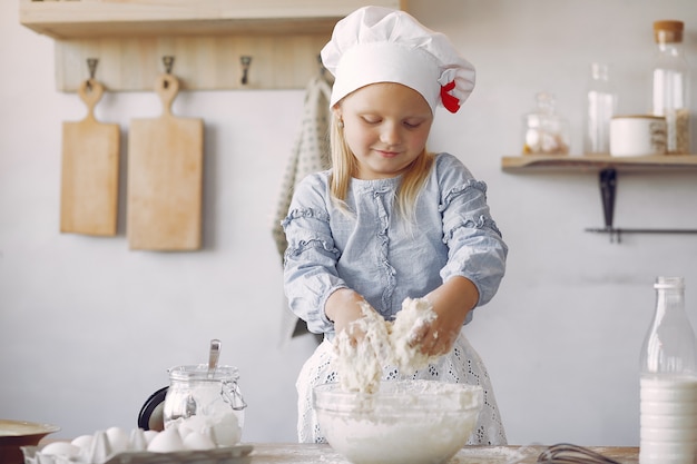 白いシェフの帽子の少女がクッキーの生地を調理します。