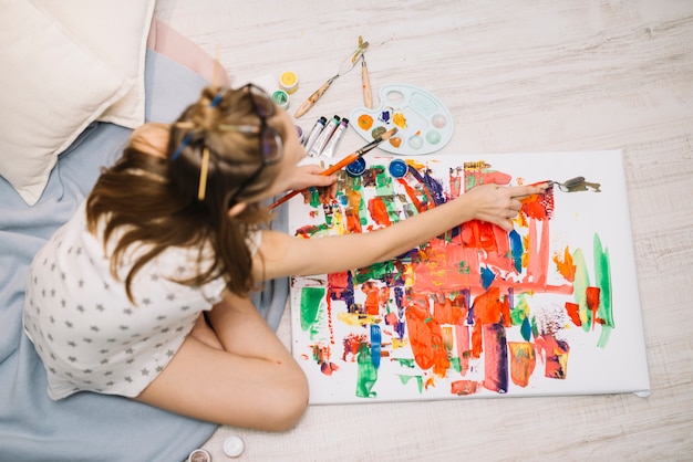 Bambina in bianco seduta sul pavimento e pittura con gouache su tela