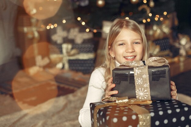 Little girl in a white sweater near christmas tree with present