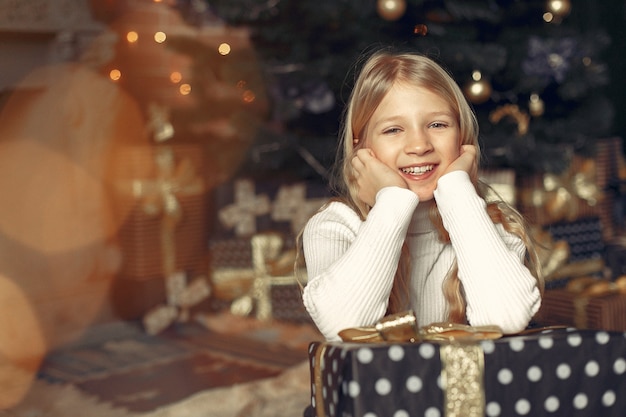 Foto gratuita bambina in un maglione bianco vicino all'albero di natale con il presente