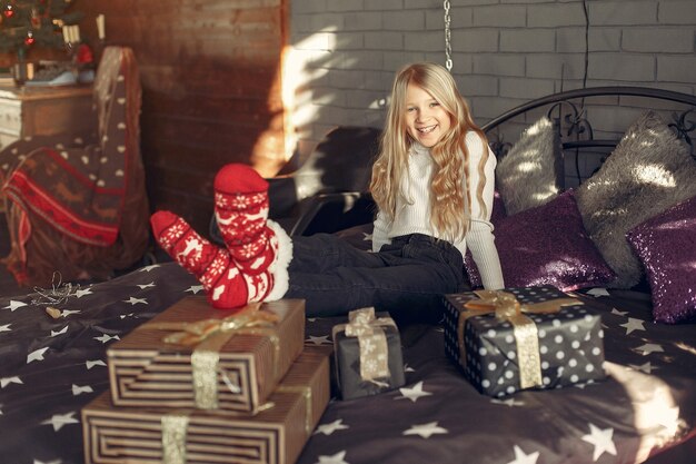 Little girl in a white sweater near christmas tree with present