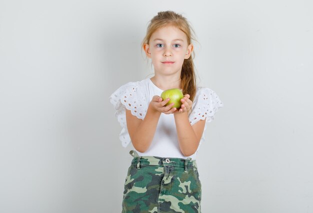 Little girl in white t-shirt, skirt holding green apple