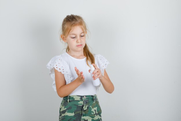 Little girl in white t-shirt, skirt pumping spray bottle to another hand and looking careful