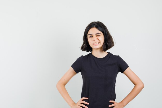 Little girl winking eye in black t-shirt and looking confident. front view.