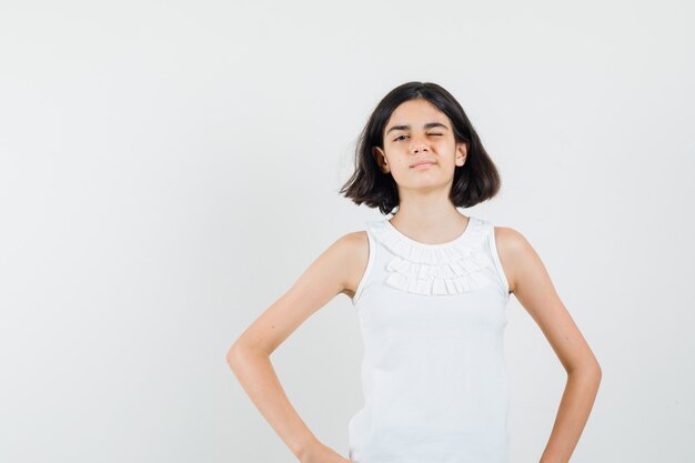 Little girl winking eye in white blouse and looking confident. front view.