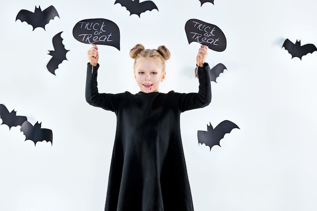 Маленькая девочка-ведьма в черном длинном платье и волшебных аксессуарах.