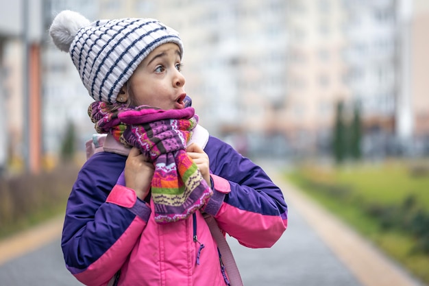 学校のコピースペースの近くにジャケットと帽子のバックパックを持つ少女