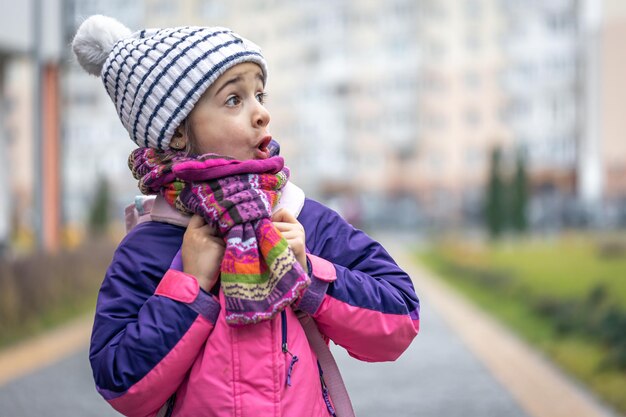 学校のコピースペースの近くにジャケットと帽子のバックパックを持つ少女