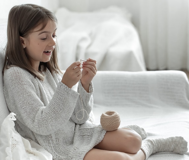 Bambina con un gomitolo di filo e un ago a casa sul divano.