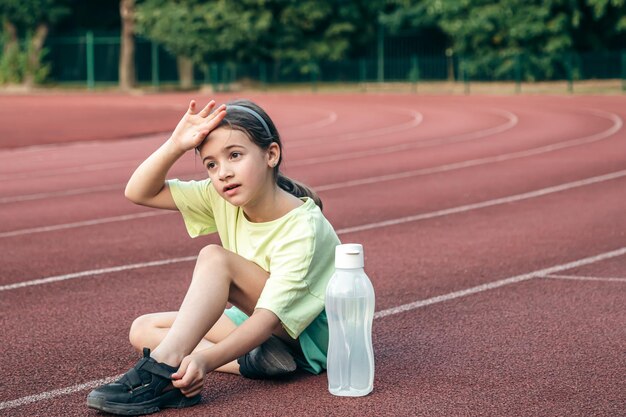 ランニング トラックに座っている水のボトルを持つ小さな女の子