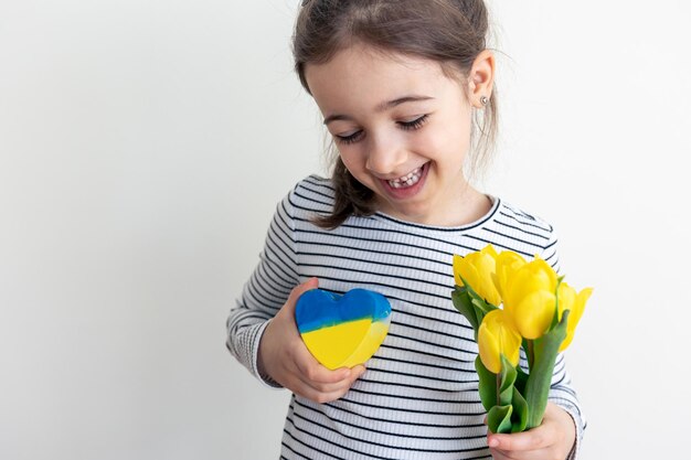 Little girl with a bouquet of tulips and a heart with the flag of ukraine
