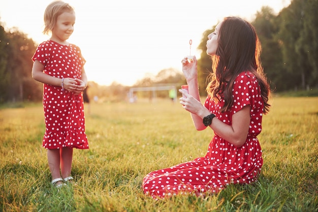 일몰 공원에서 그녀의 어머니와 함께 거품을 가진 어린 소녀.