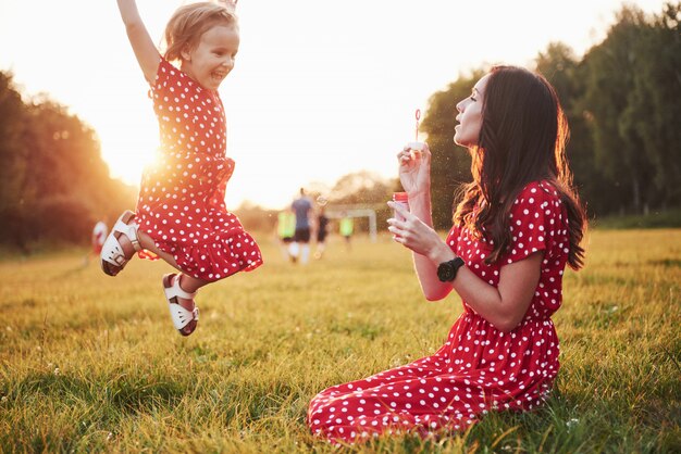 Маленькая девочка с пузырьками с матерью в парке на закате.