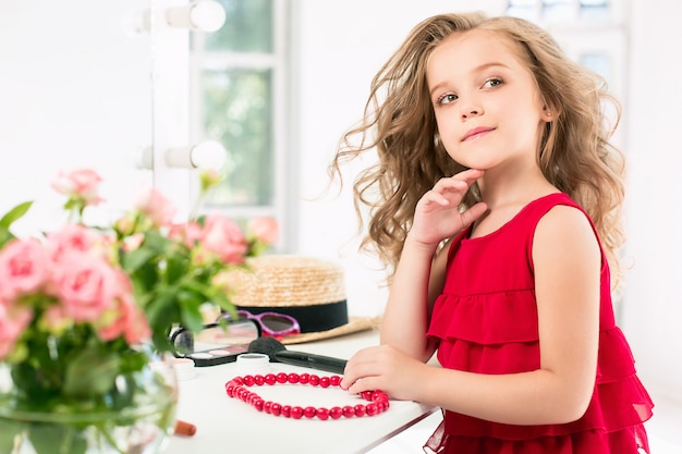 A little girl with cosmetics. She is in mother's bedroom, sitting near the mirror.