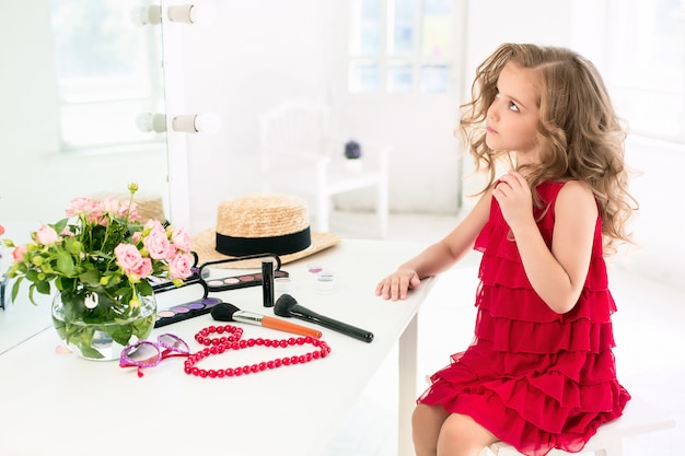 Free photo a little girl with cosmetics sitting near the mirror.