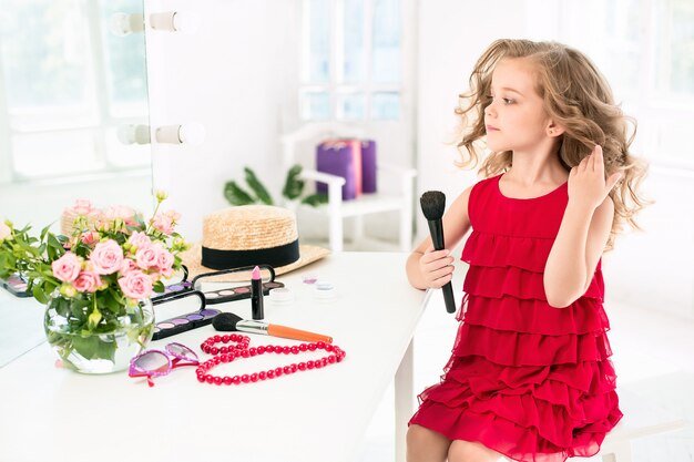 A little girl with cosmetics sitting near the mirror.