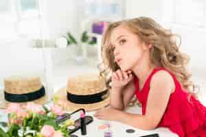 Free photo a little girl with cosmetics sitting near the mirror.